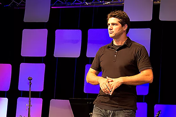 Joshua Becker on stage at a speaking event wearing a black polo shirt and jeans.