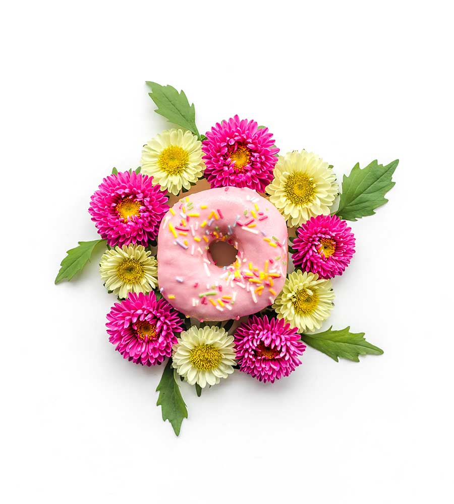 pink frosted donut with sprinkles surrounded by pink and yellow flowers.