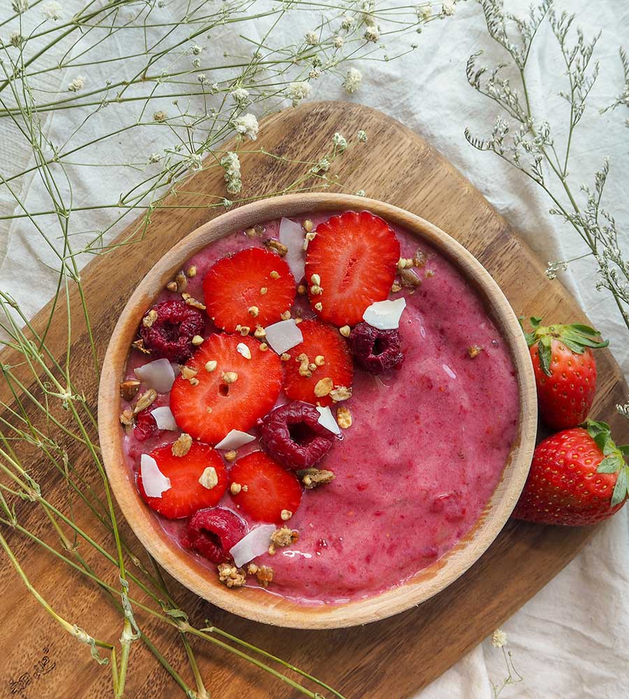 smoothie bowl topped with raspberries, strawberries, and coconut shavings.
