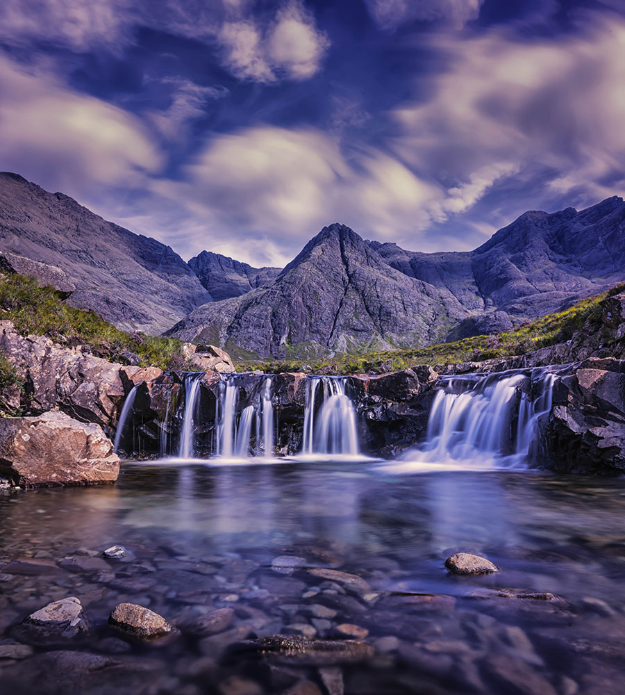 a short drop waterfall into a stream with mountains in the background.
