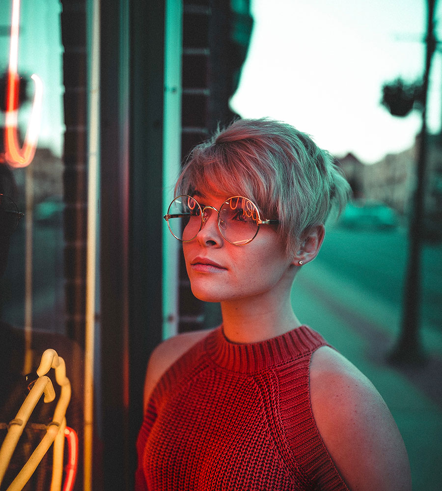 womanm with pixie haircut, red shirt, and large circle glasses looking into a store window.