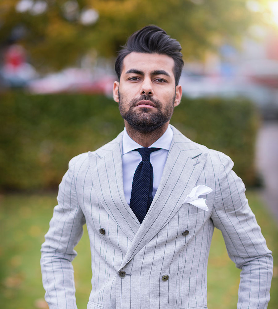 man wearing a pin-striped suit standing in grass with a serious expression.